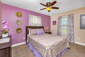 Une chambre à coucher comprenant un lit, un ventilateur de plafond, des œuvres d’art décoratives au mur et une table de chevet avec une lampe.