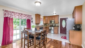 A kitchen with wooden cabinets, a dining table with chairs, a microwave, an oven, and a refrigerator. - The Haven, located in the heart of the Shenandoah Valley (Waynesboro)