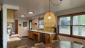 A modern kitchen with wooden cabinets, a large island, and a dining area with a wooden table. - Lakefront Cottage with Private Beach, Sleeps 14 (Newaygo)