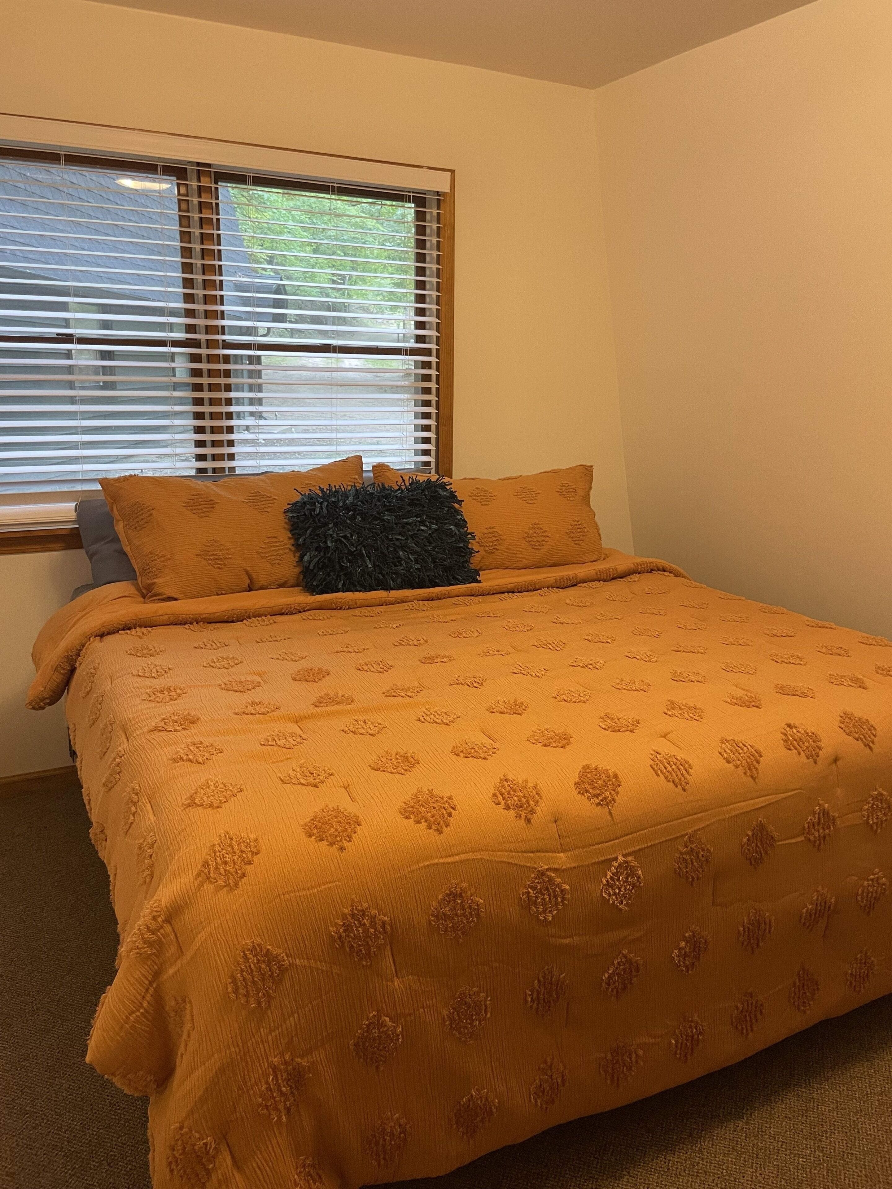 Een slaapkamer met een groot bed, een raam met zonwering en uitzicht op groen.