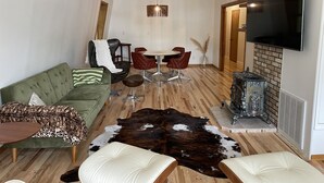 A modern living room with a green sofa, leather chairs, a wooden coffee table, a leather ottoman, a cowhide rug, a fireplace, and a flat-screen TV. - Lakefront Cottage with Private Beach, Sleeps 14 (Newaygo)