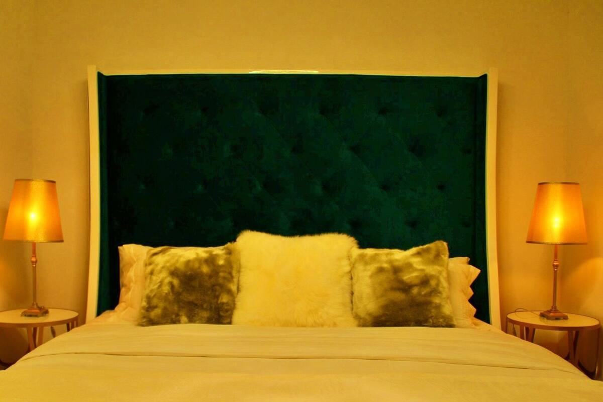 A bed with a green upholstered headboard, two bedside lamps, and two pillows.