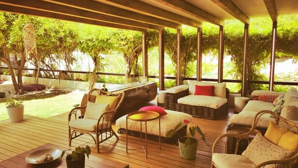 An outdoor covered patio with wicker furniture, a dining table, and potted plants.