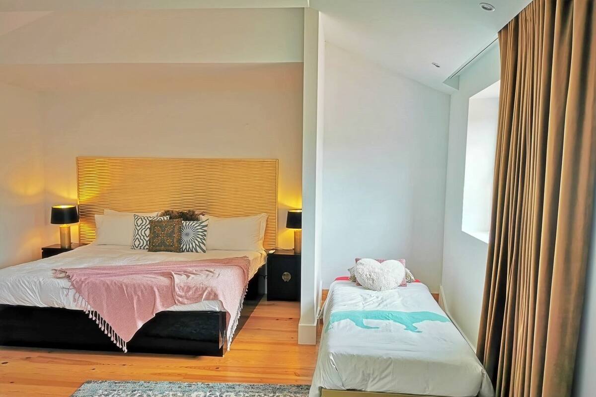 A bedroom with two beds, a wooden headboard, and a large window with curtains.