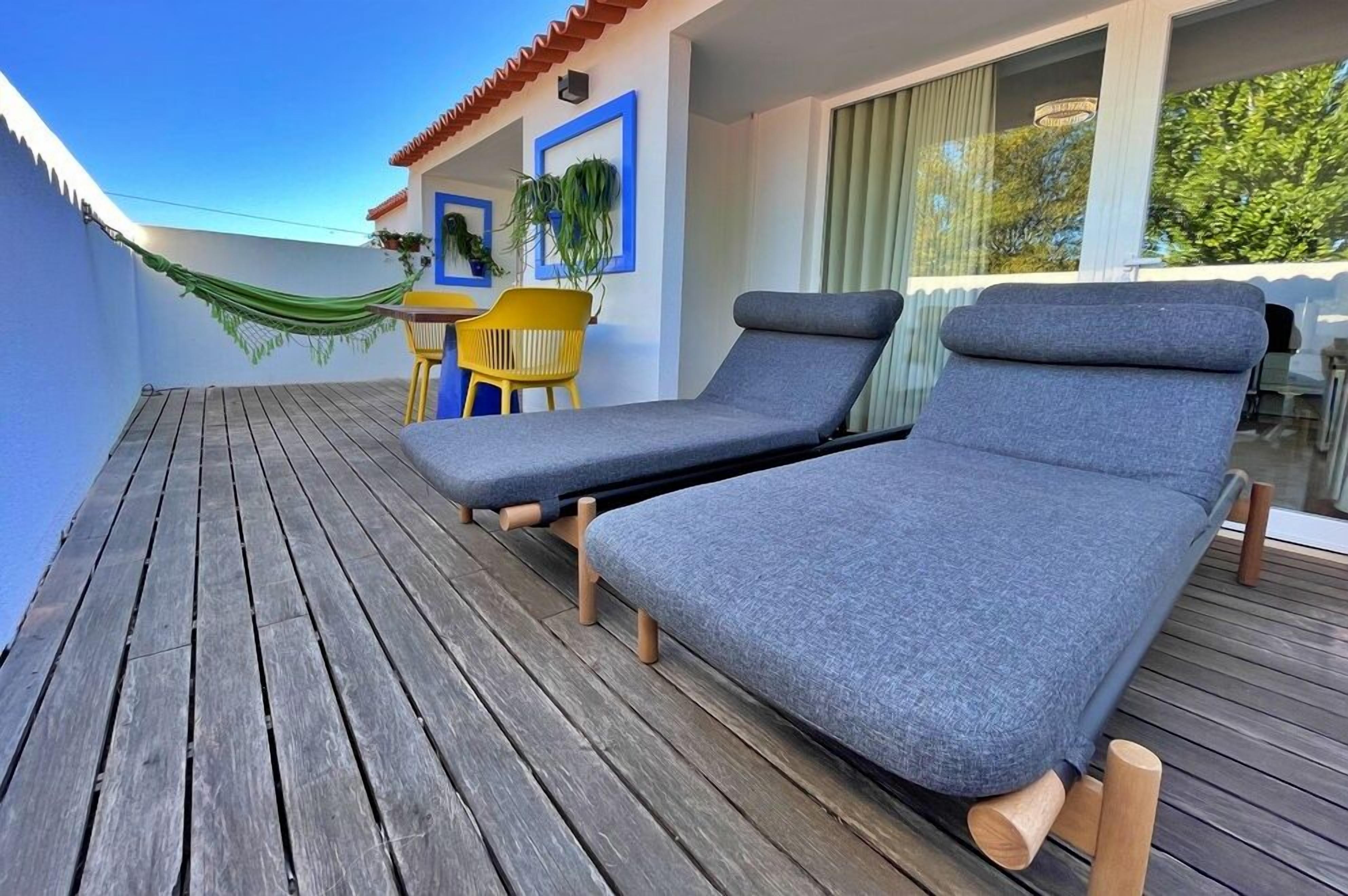 Un pontile di legno con due poltrone da relax e una sedia gialla, un'amaca e un tavolo con sedie.