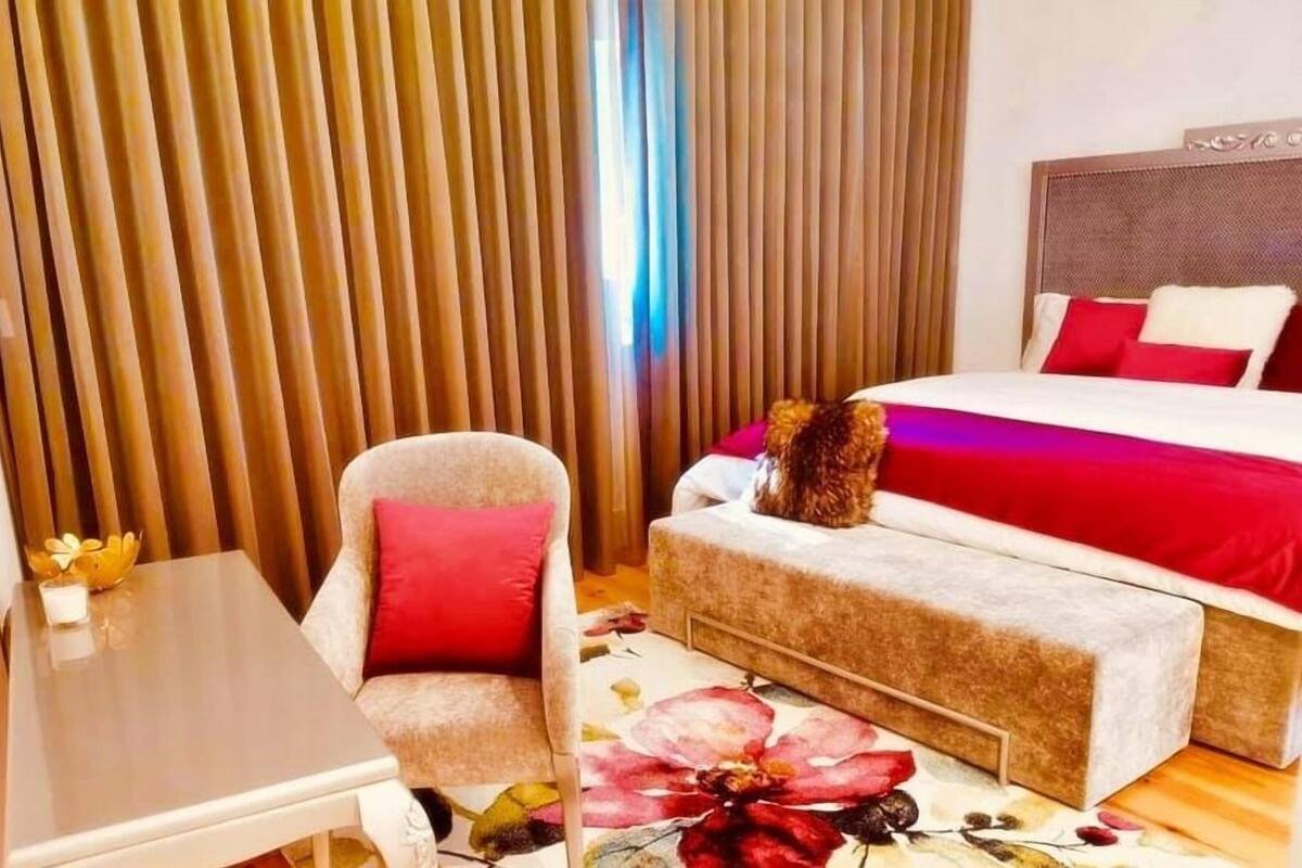 A hotel room with a bed, a chair, a small table, and a window with curtains.