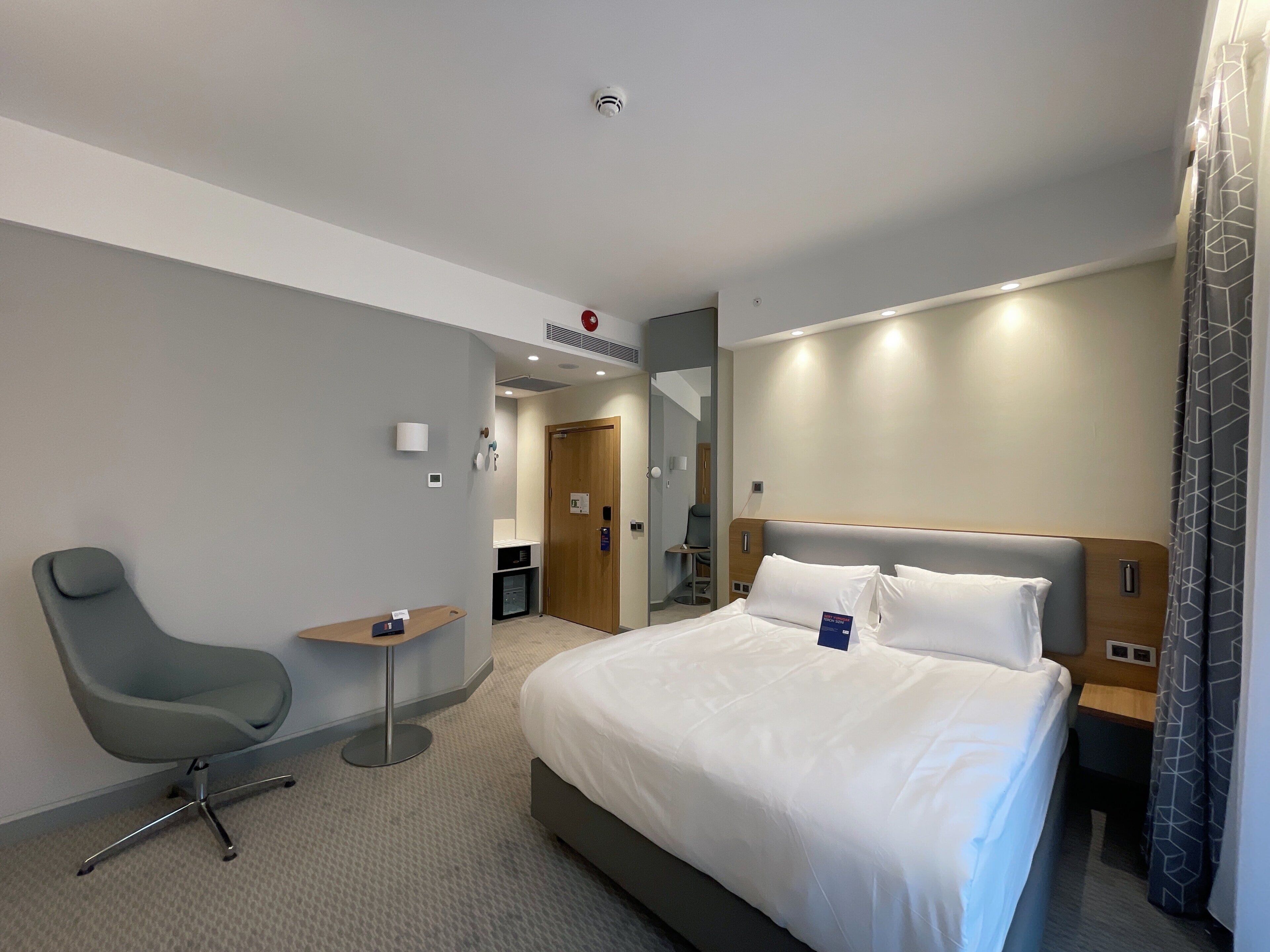 Een hotelkamer met een groot bed, een bureau, een stoel en een badkamer die door een open deur zichtbaar is.