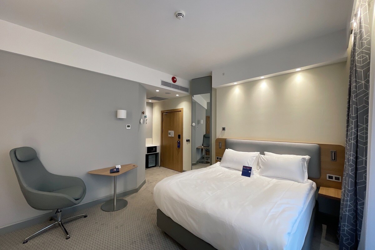 A hotel room with a large bed, a desk, a chair, and a bathroom visible through an open door.