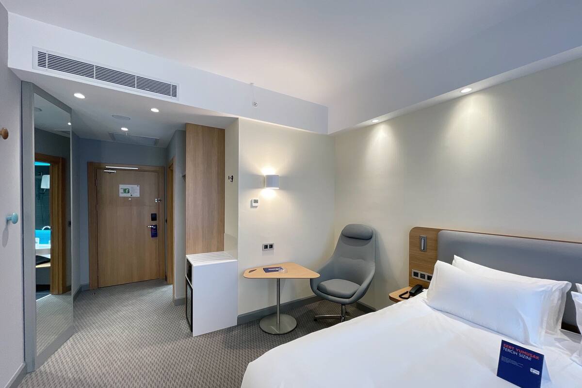 A hotel room with a bed, a chair, a small table, and a desk.