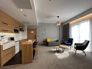 A modern hotel room with a kitchenette, a sofa, two armchairs, a coffee table, and large windows with curtains. - Holiday Inn Express Ankara Airport by IHG (Akyurt)