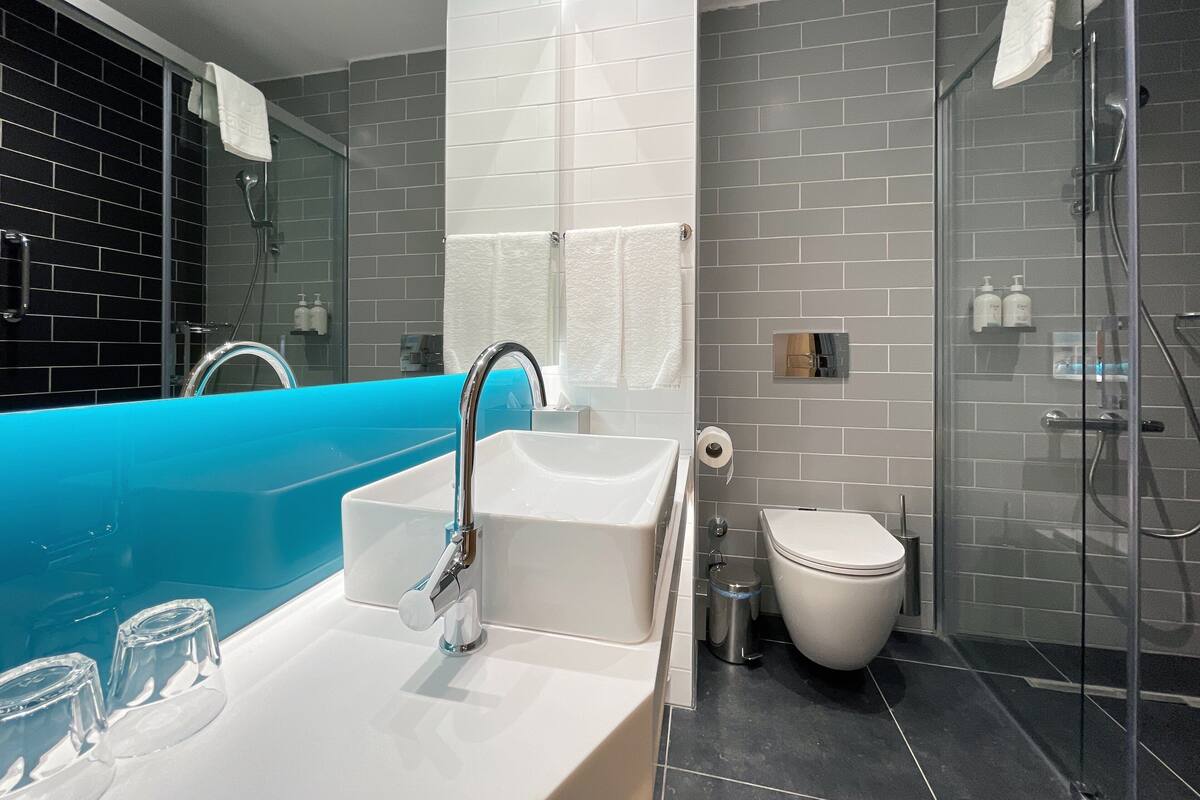 A modern bathroom with a blue bathtub, a white sink, and a glass-enclosed shower area.