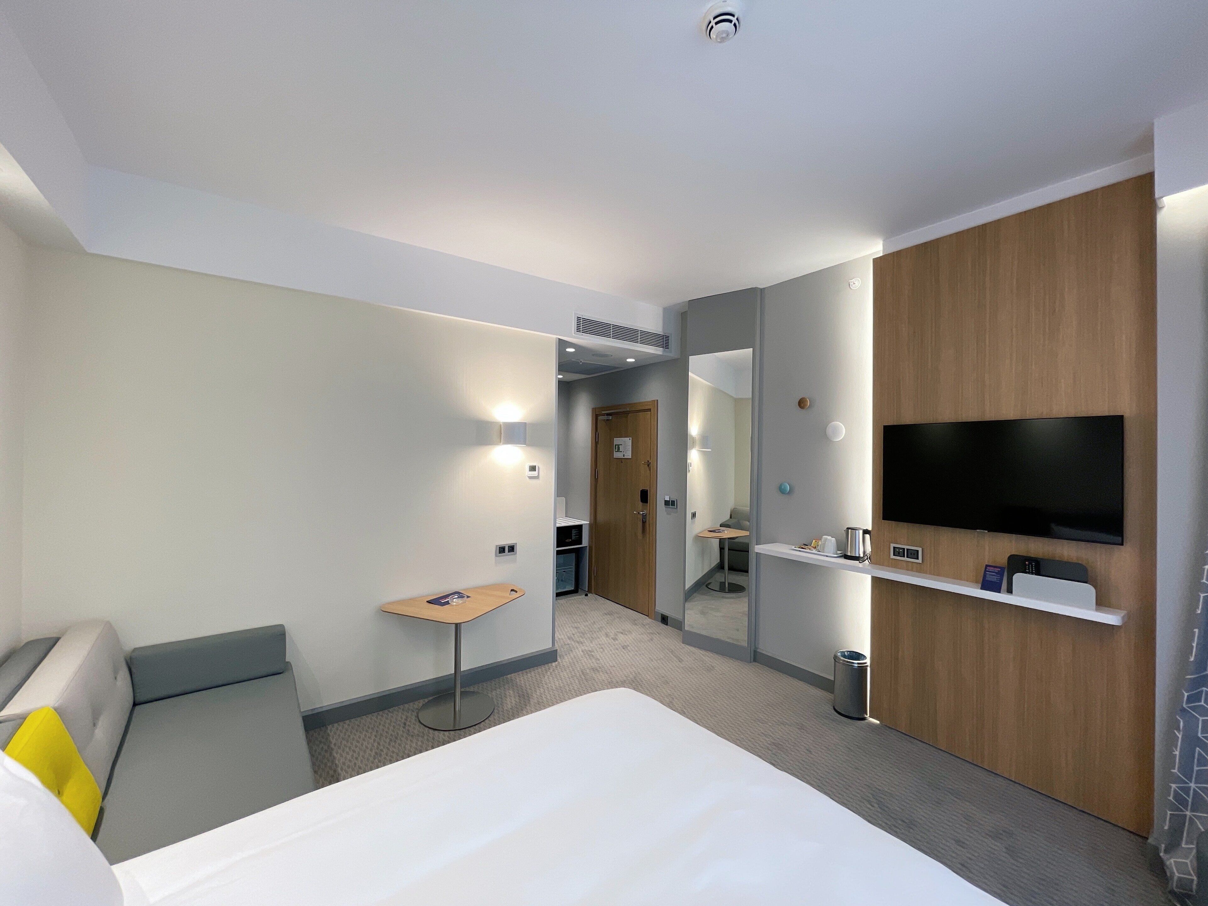 A hotel room with a bed, a desk, a TV, and a mirror.