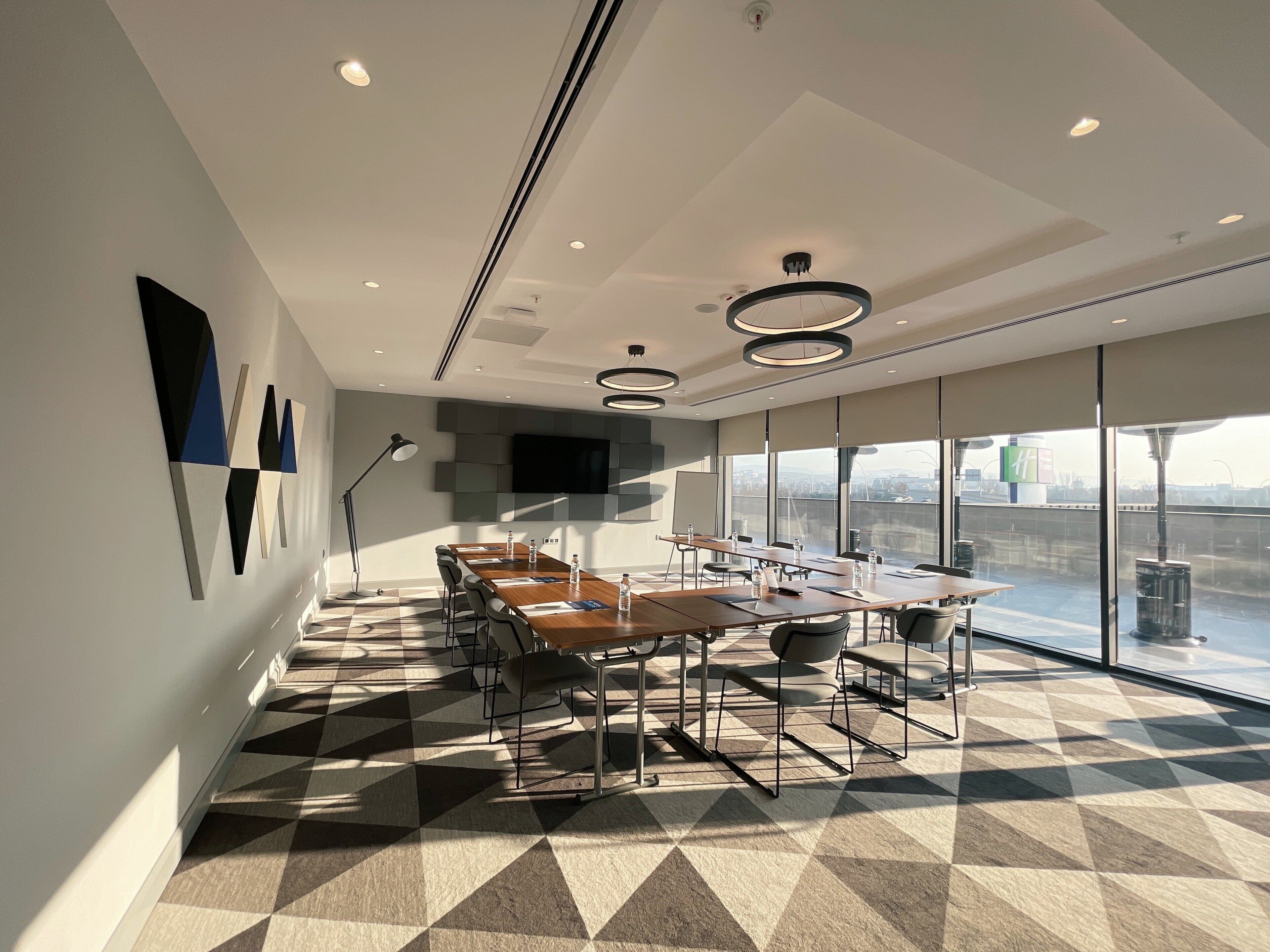 Una sala de conferencias moderna con una mesa grande, sillas, un televisor de pantalla plana y vistas a la ciudad a través de amplias ventanas.