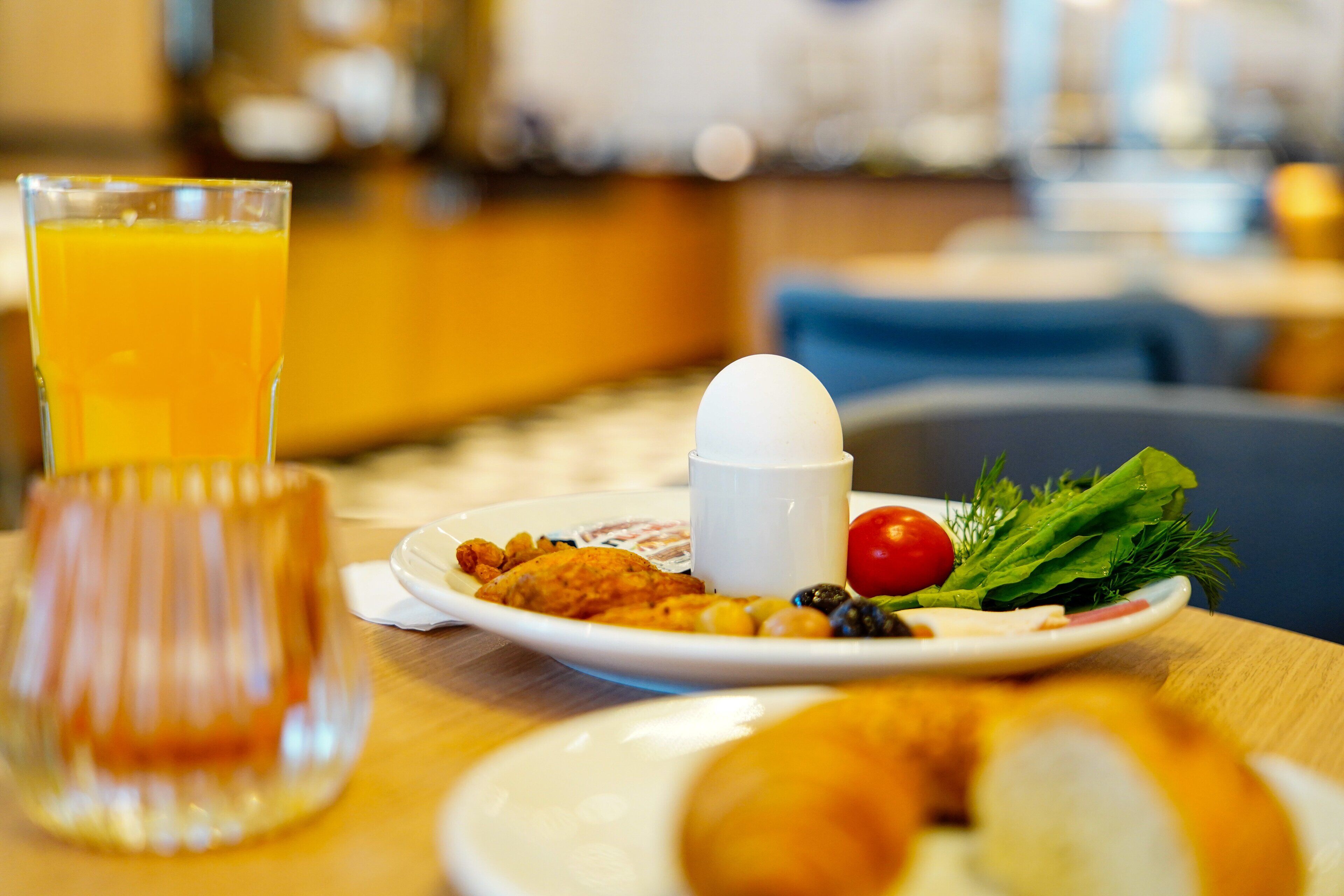 Un desayuno con un vaso de jugo de naranja, un plato de comida que incluye huevos, verduras y pan, y una taza blanca.
