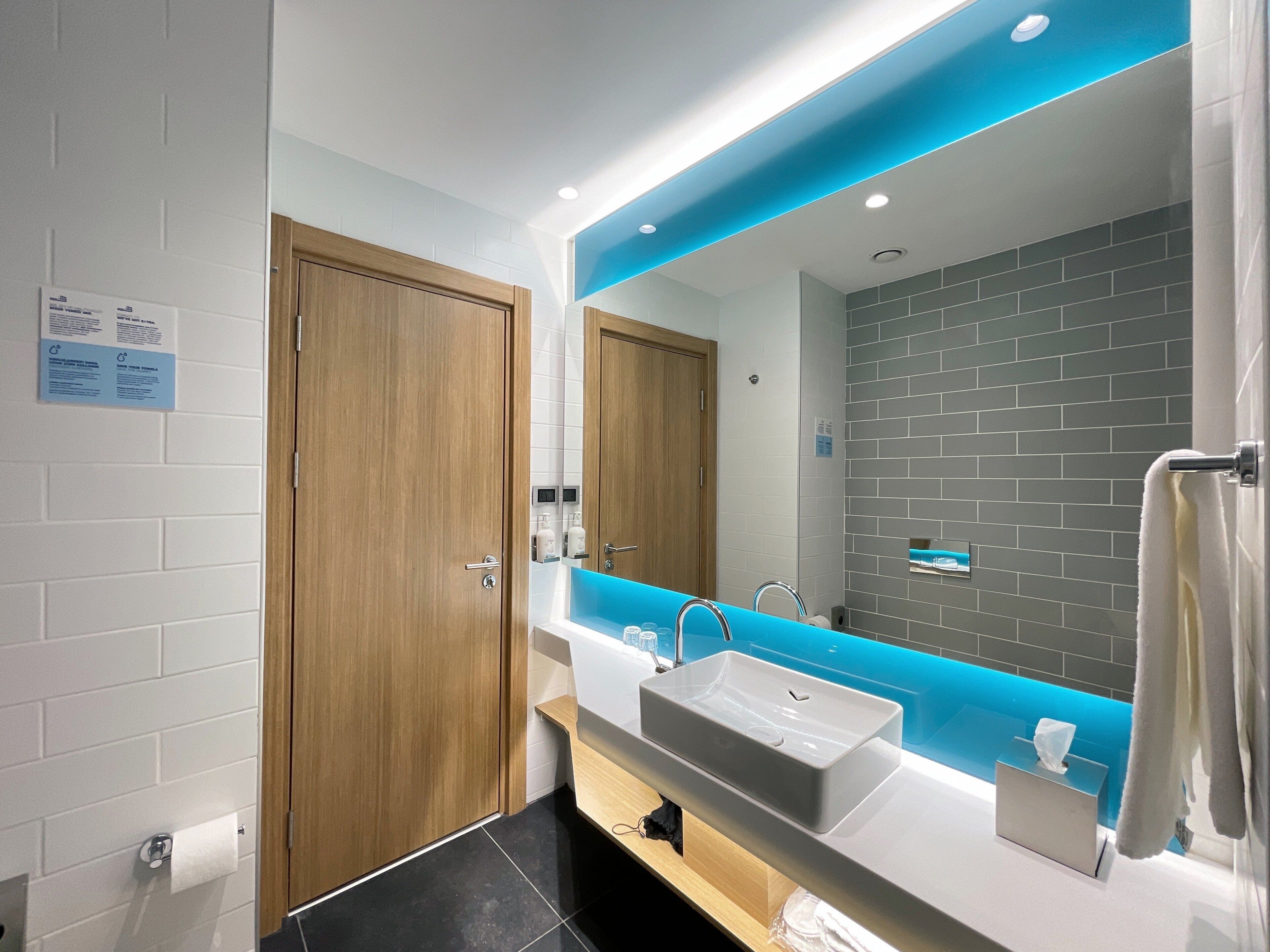 A modern bathroom with a large mirror, a sink, and a wooden door.