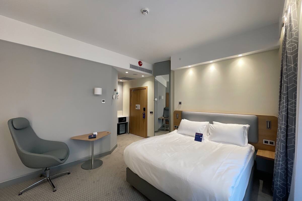 A hotel room with a large bed, a desk, a chair, and a bathroom visible through an open door.
