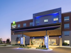 A Holiday Inn Express & Suites building with a modern design, featuring a prominent entrance, stone pillars, and a well-lit facade.