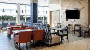 A modern dining area with high tables and booths, large windows, and a flat-screen TV mounted on the wall. - Holiday Inn Express and Suites Meridian-Boise west by IHG (Meridian)