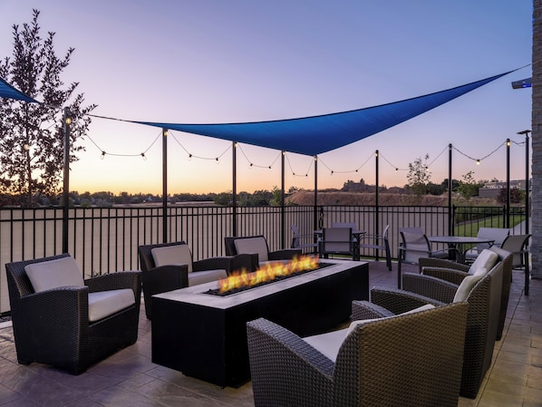 An outdoor patio with wicker furniture, a fire pit, and string lights.