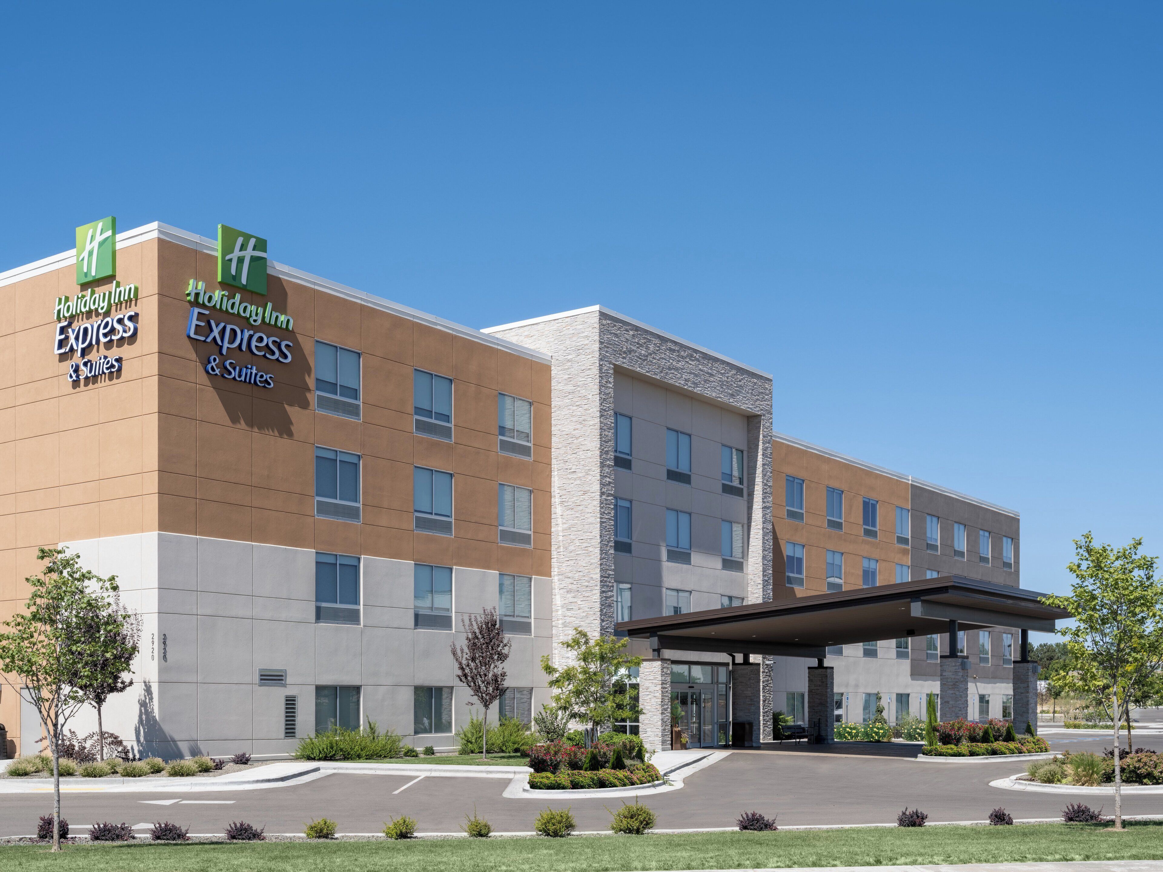 A Holiday Inn Express & Suites hotel with a modern design, featuring a large parking lot and landscaped areas.