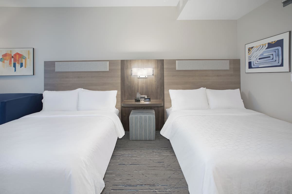 A hotel room with two beds, a small table with a lamp, and artwork on the walls.