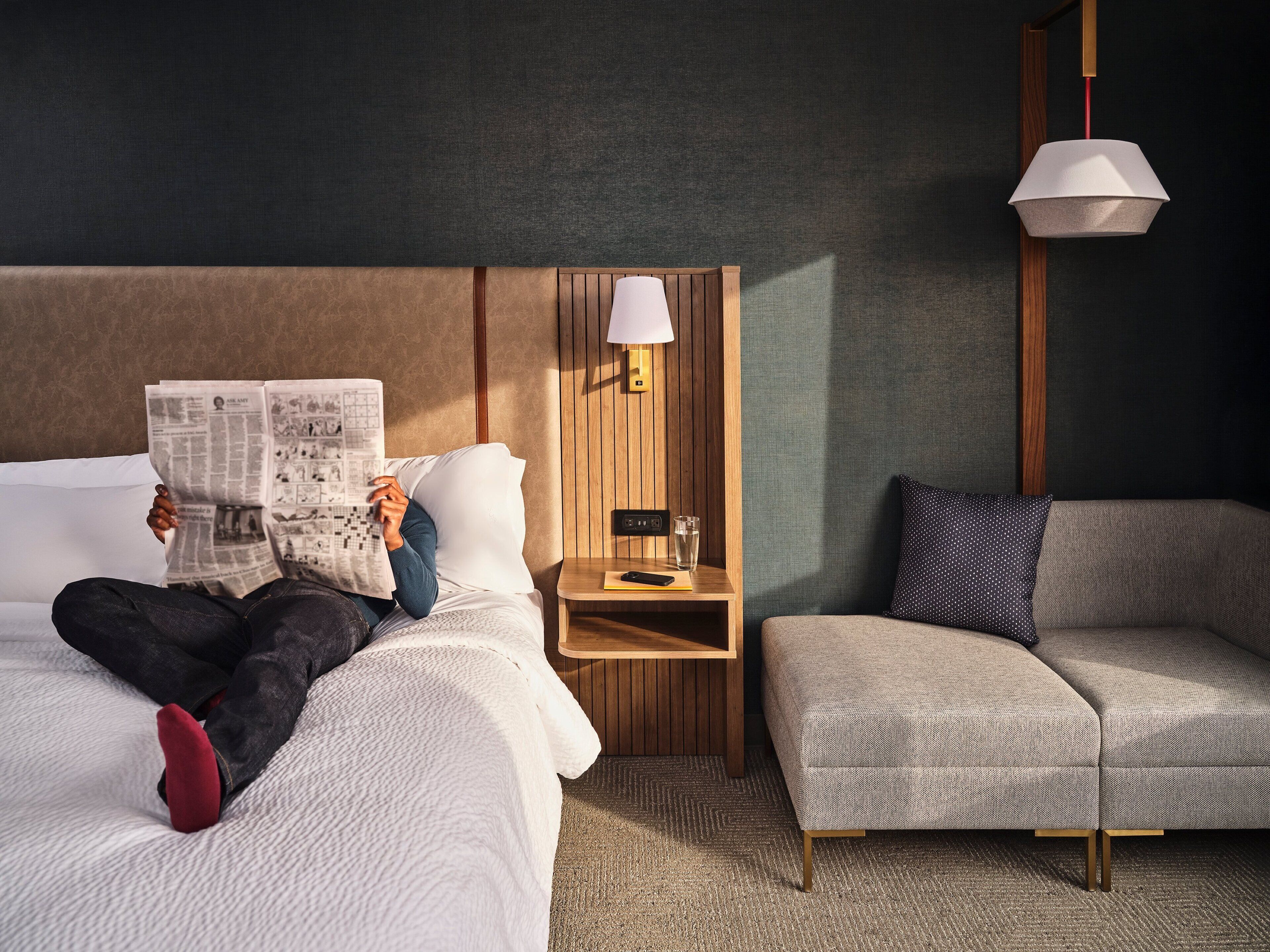 Una habitación de hotel con una cama, un área de lectura con una lámpara y un sofá.