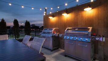 An outdoor patio with two barbecue grills, a table, and chairs.