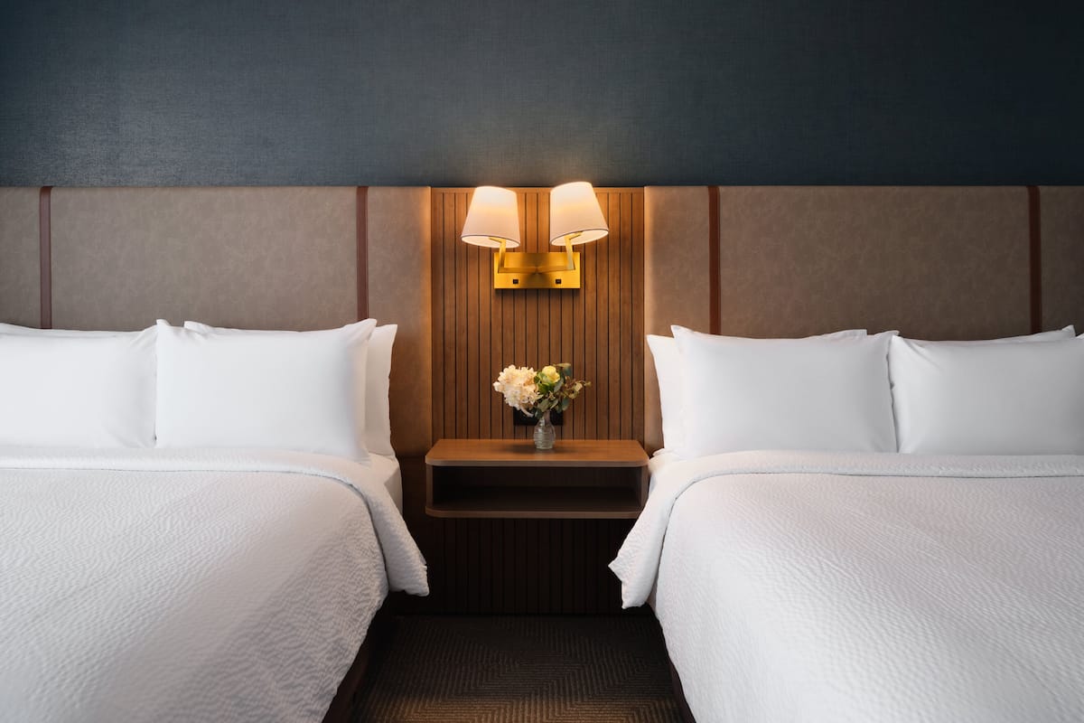 Ein Hotelzimmer mit zwei Betten, einem Nachttisch mit Blumenvase und Wandlampen.