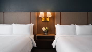 Habitación de hotel con dos camas, una mesita de noche con un florero y lámparas fijadas a la pared.
