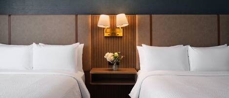 A hotel room with two beds, a nightstand with a vase of flowers, and wall-mounted lamps.
