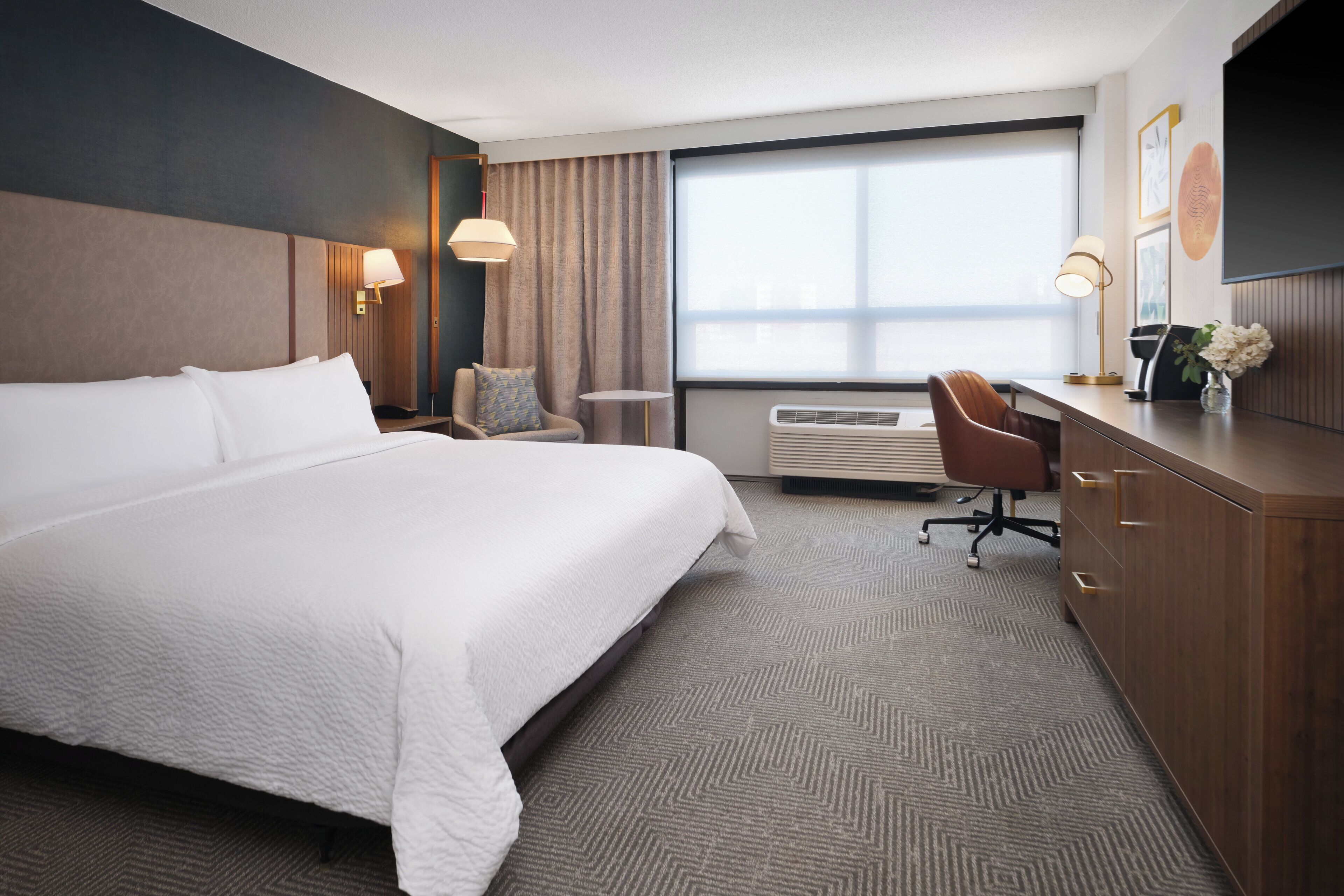 Habitación de hotel con una cama grande, un escritorio, una silla, un equipo de aire acondicionado y una ventana con cortinas.