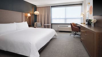 Habitación de hotel con una cama grande, un escritorio, una silla, un equipo de aire acondicionado y una ventana con cortinas.