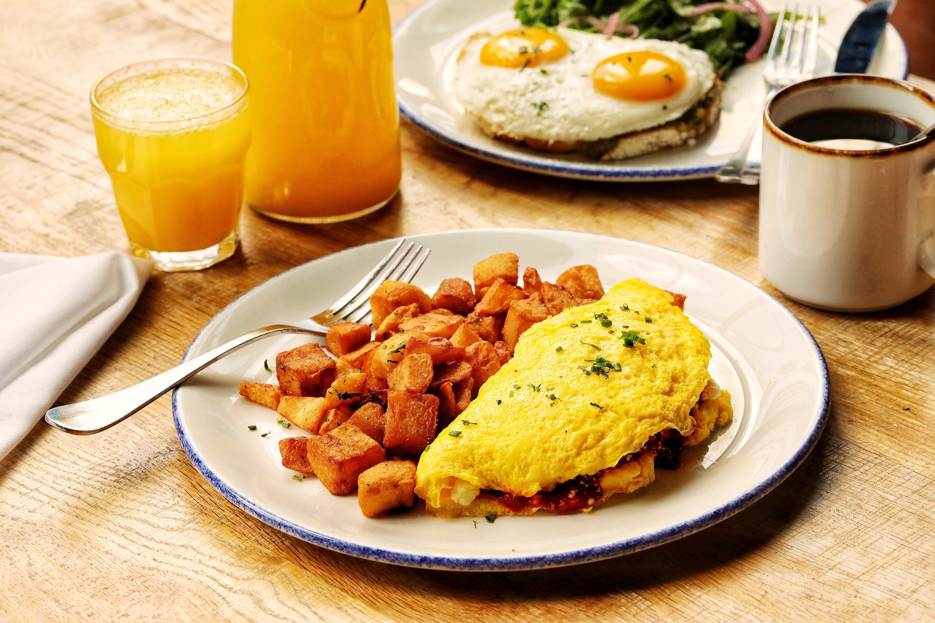 A breakfast plate with an omelet and potatoes, a glass of orange juice, and a cup of coffee on a wooden table.