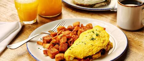 A breakfast plate with an omelet and potatoes, a glass of orange juice, and a cup of coffee on a wooden table.