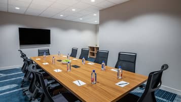 Un salón de conferencias con una larga mesa, sillas, botellas de agua y una pantalla.