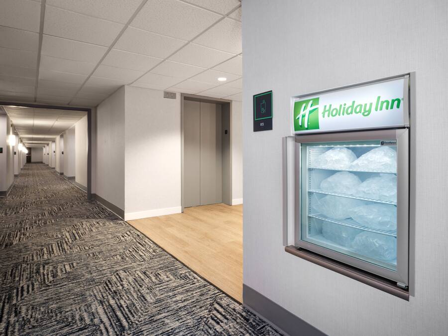 Un pasillo de hotel con un letrero de Holiday Inn, una máquina de hielo y piso alfombrado.