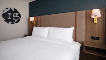 A hotel room with a large bed, two bedside lamps, a wall art piece, and a wooden panel wall.