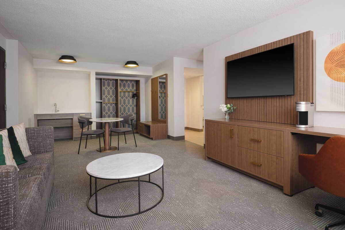 Een moderne woonkamer met een bank, een ronde salontafel, een televisie en een keuken op de achtergrond.