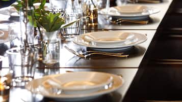 A dining table set with plates, glasses, and cutlery, accompanied by small potted plants.