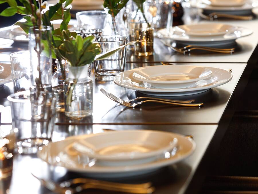 A dining table set with plates, glasses, and cutlery, accompanied by small potted plants.