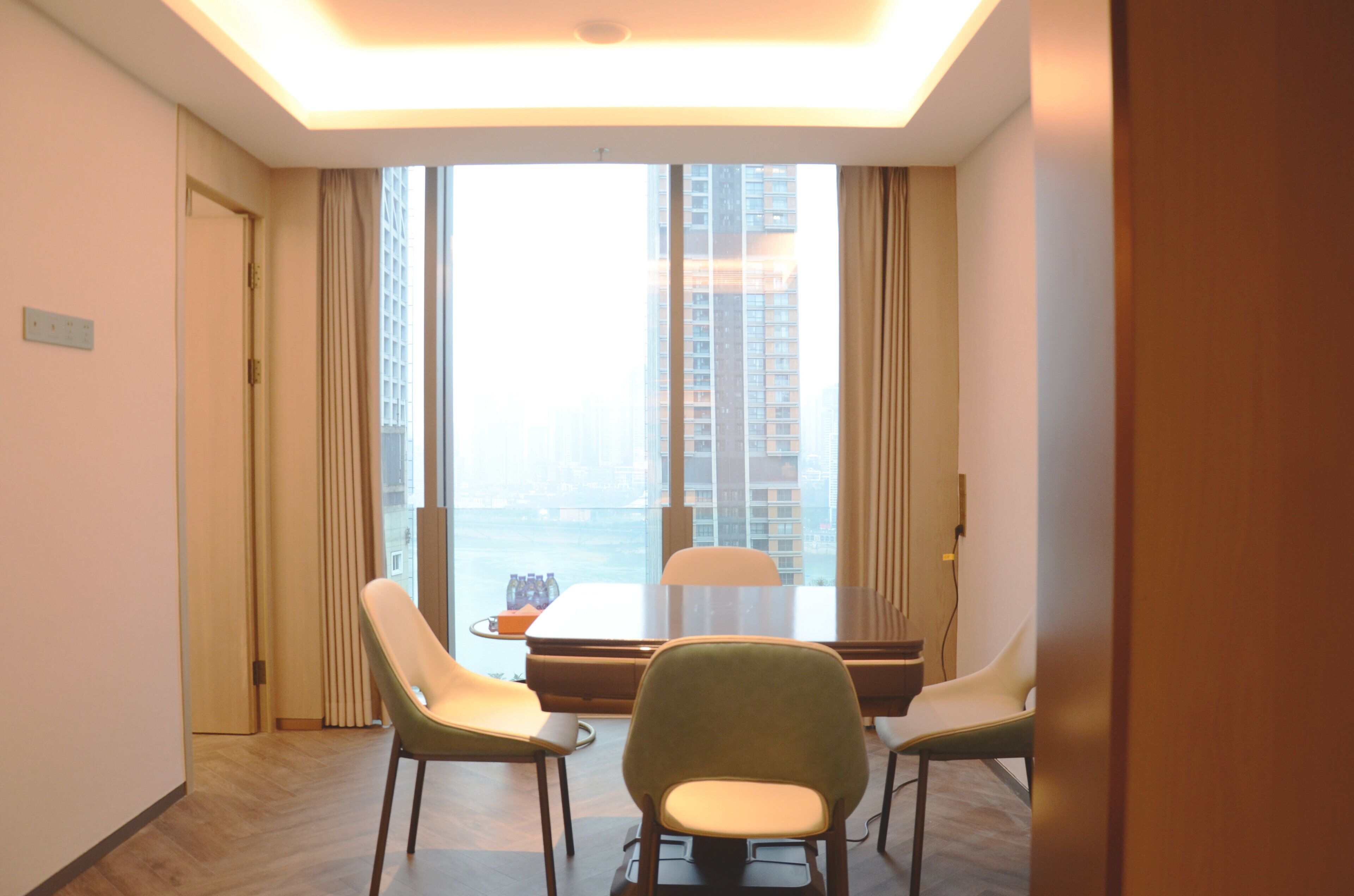 Une chambre d’hôtel dotée d’une grande fenêtre, d’une table à manger avec des chaises et offrant une vue sur de hauts immeubles.