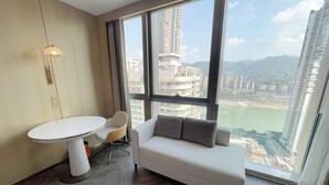 A modern hotel room with a large window, a white sofa, a round table, and a lamp. - voco Chongqing Chaotianmen by IHG (Chongqing)