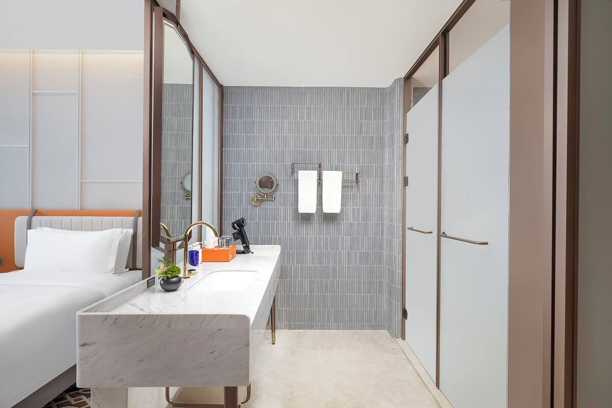 A modern hotel room with a large bed, a marble bathroom counter, a sink, and a mirror.