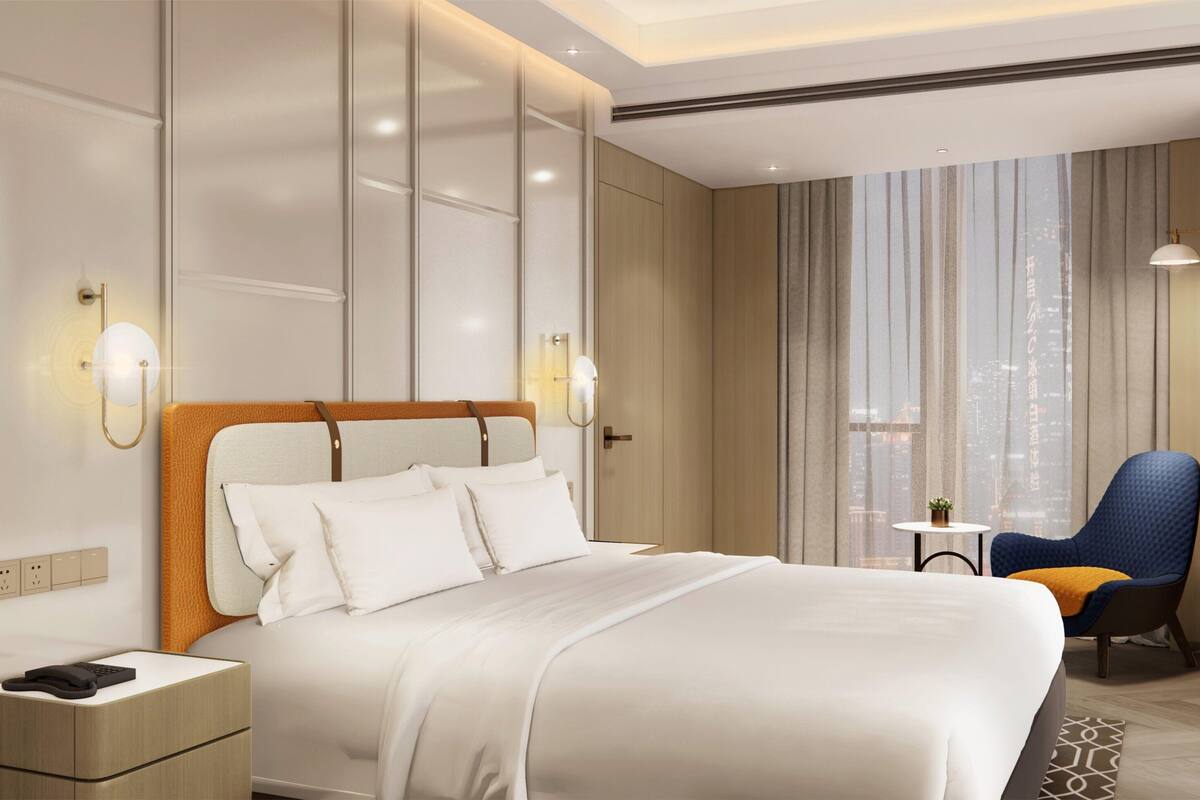 A hotel room with a large bed, a nightstand, a chair, and a view of the city through the window.