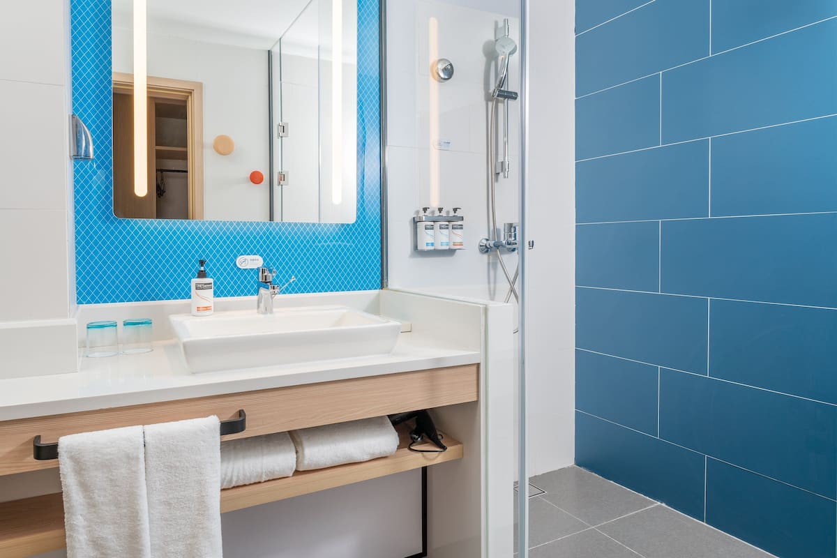 A modern bathroom with a white sink, blue-tiled shower, and a wooden vanity.