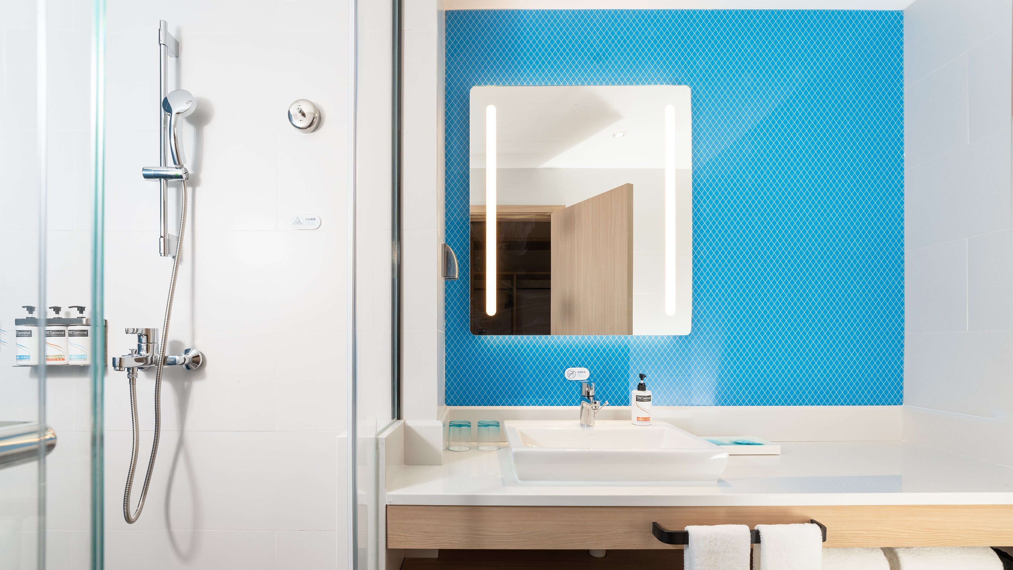 A modern bathroom with a glass shower enclosure, a white sink, and a blue tiled backsplash.