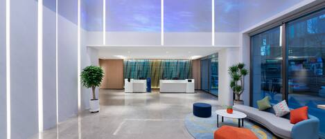 A modern lobby with a reception desk, seating area, and large windows offering a view of the street.