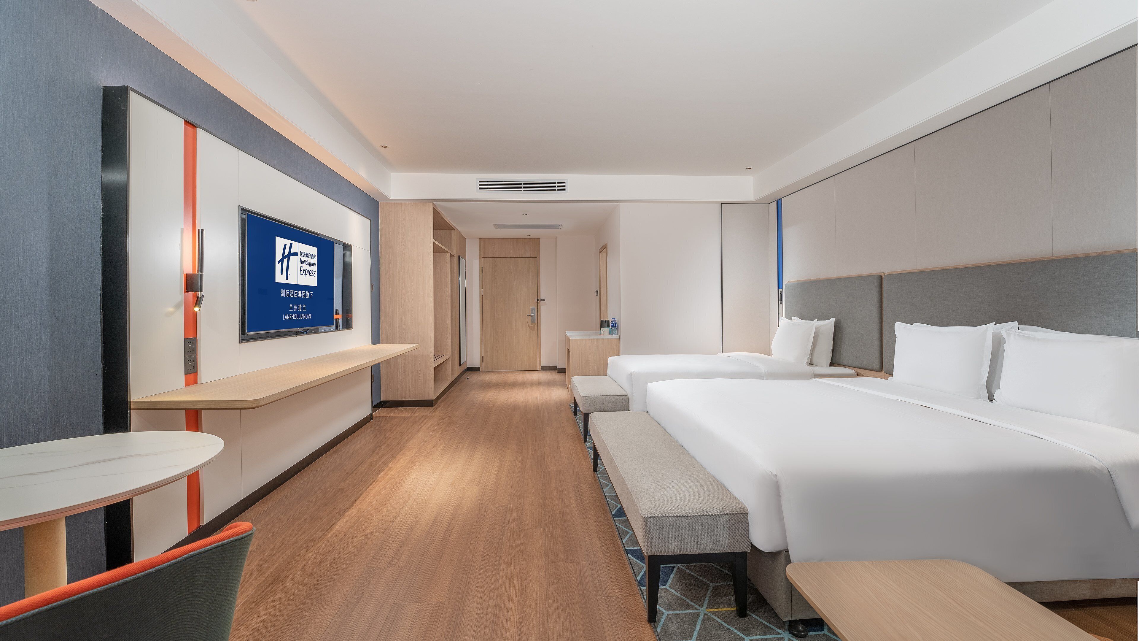 A hotel room with a bed, bedside tables, a desk, and a TV displaying a sign.
