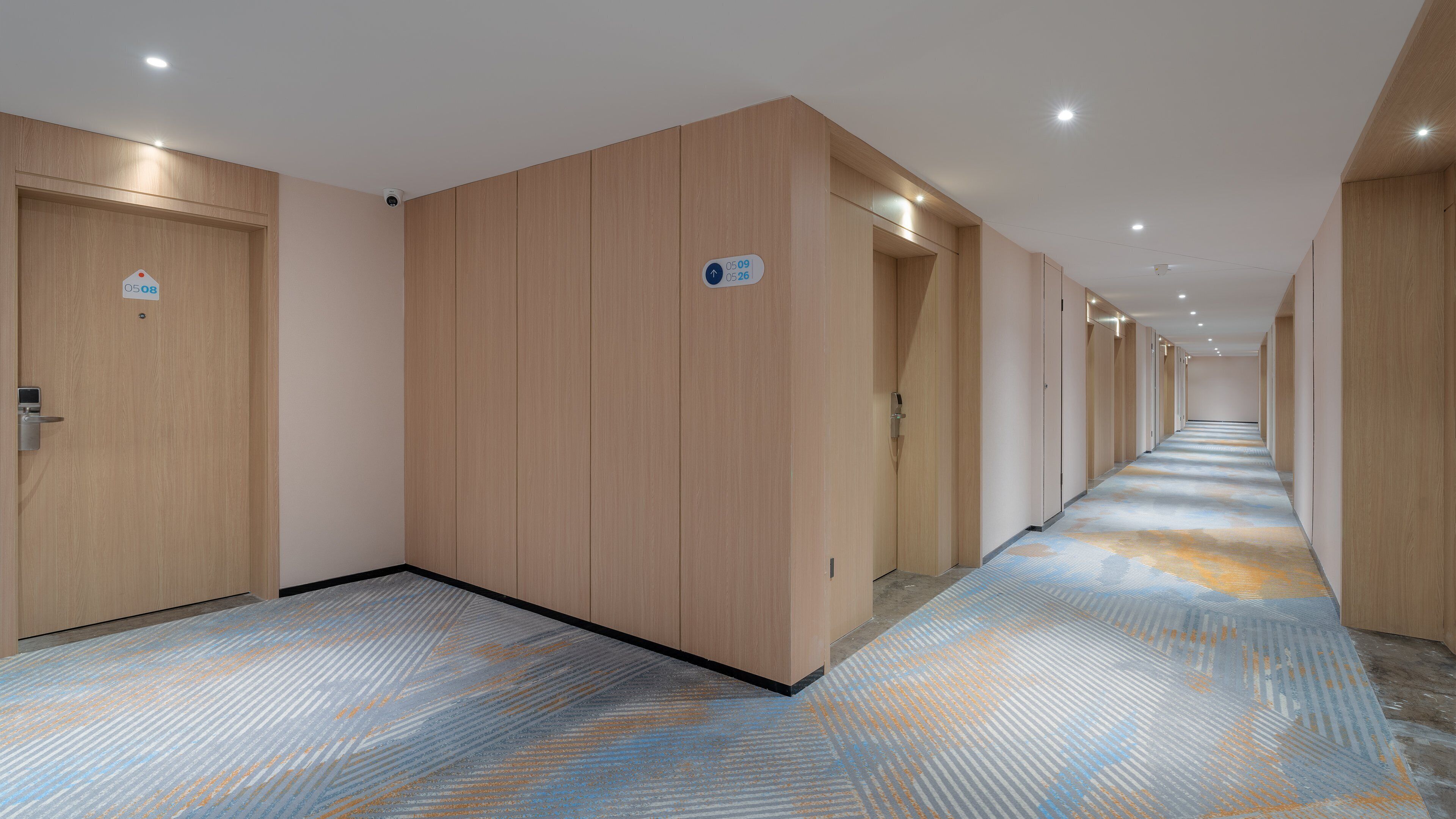 Een hotelgangen met houten deuren, een kamer met een patroon tapijt en een bordje met kamer nummers.