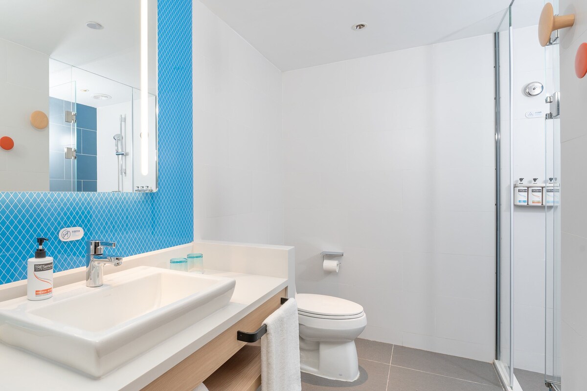 A modern bathroom with a large mirror, two sinks, a toilet, and a shower area.
